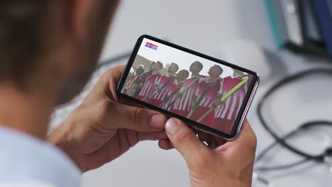 compuesto de un médico masculino viendo un partido de hockey en un teléfono inteligente