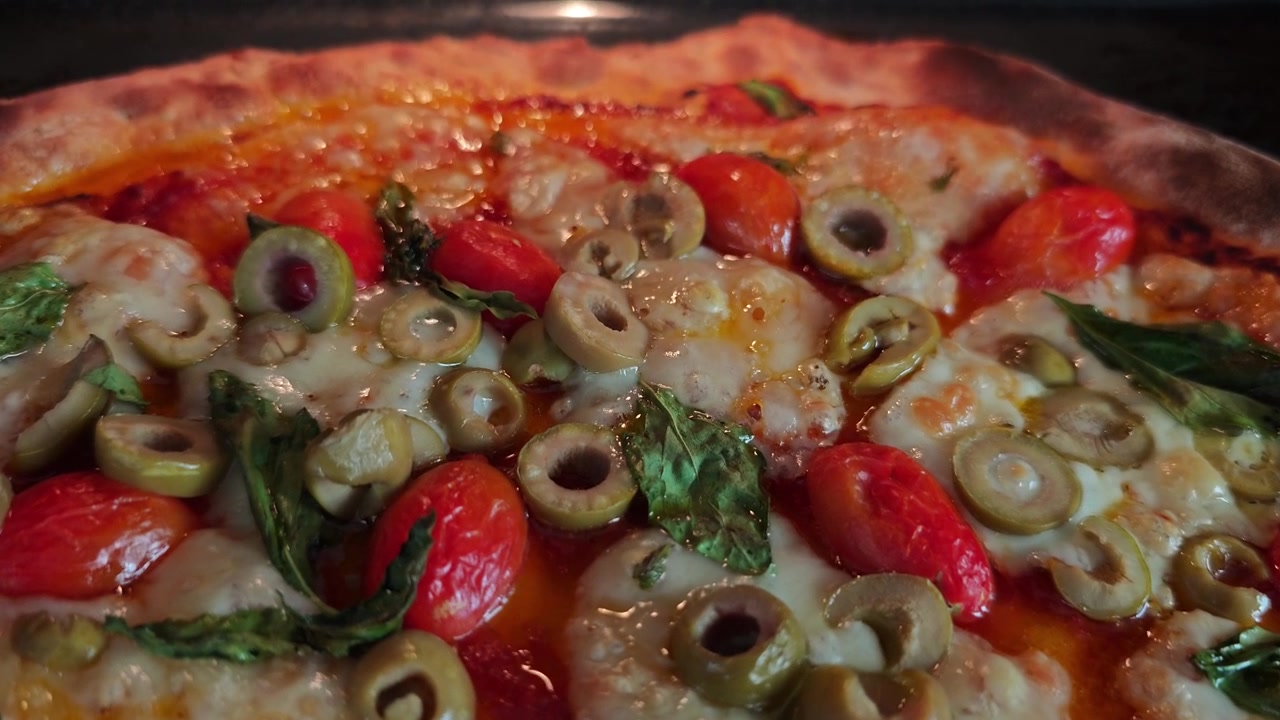 Primo piano in Ultra Slow Motion 4K di pizza fatta in casa che cuoce nel forno, salsa di pomodoro che bolle, formaggio fuso, olive nere, pomodorini e foglie di basilico fresco che creano delizioso cibo italiano cinematografico. HD