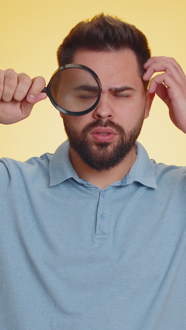 Investigator researcher man with magnifying glass near face looking into camera with big zoom eye