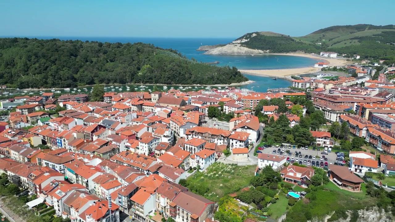 Vista aerea con drone di una piccola città di campagna spagnola con un fiume e un ponte bianco, circondata da una montagna verde a Plentzia