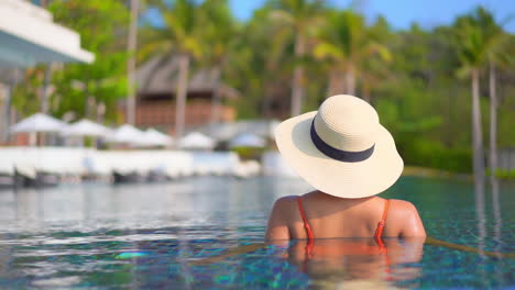 Back-of-Unrecognizable-fit-girl-standing-in-swimming-pool-water-in-a-tropical-hotel-in-the-Bahamas,-copy-space