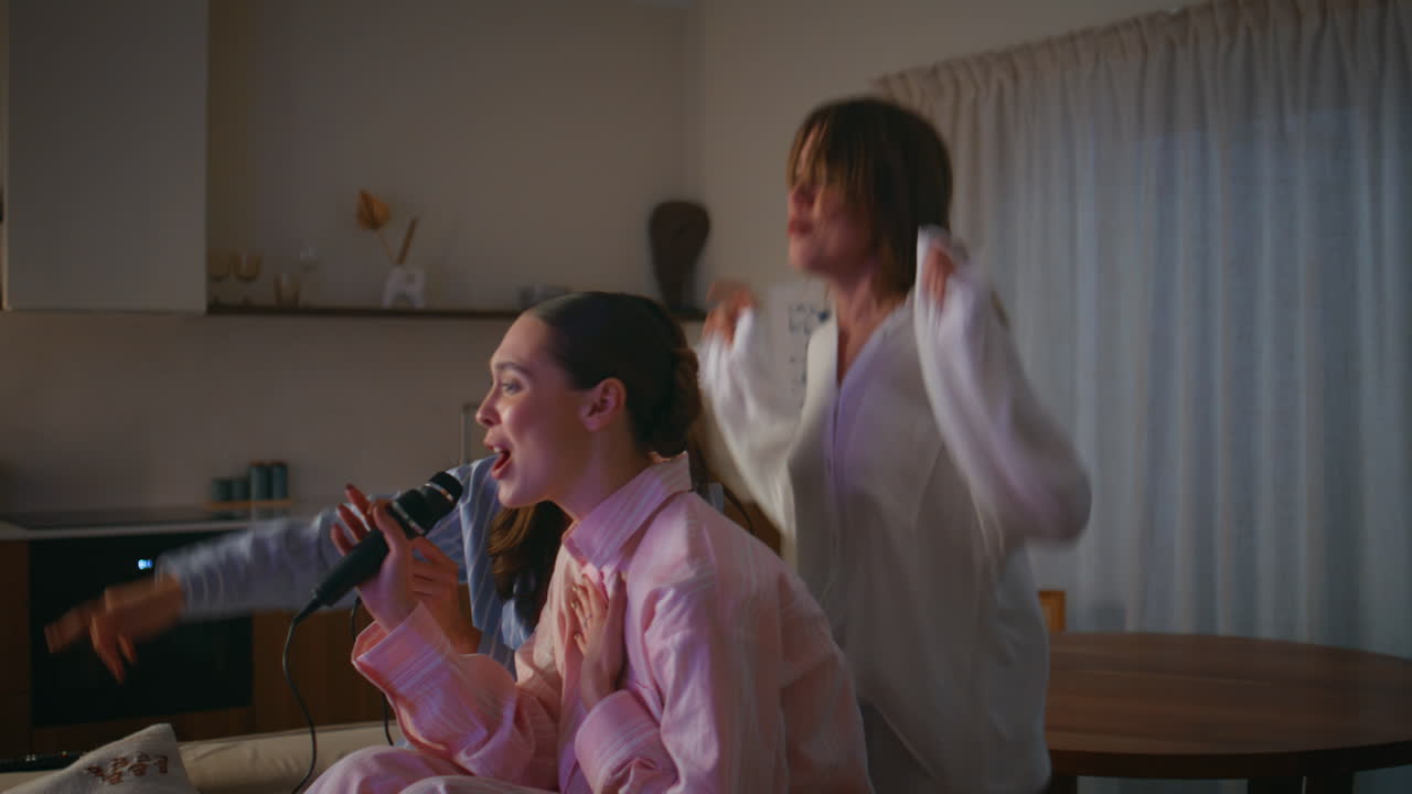 Pajamas friends enjoy karaoke at home sleepover closeup. Playful girls singing