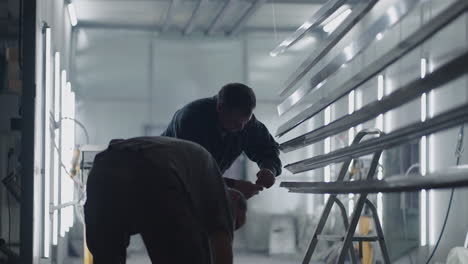 two male painters prepare steel metal elements for painting by fixing them on suspensions. painting shop. slow-motion filming.