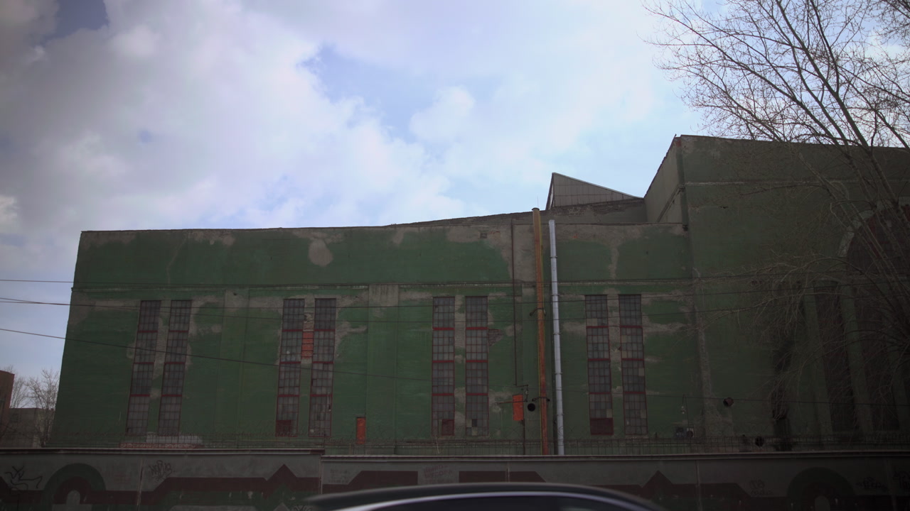 Green Warehouse Facade Under Cloudy Sky, Weathered Industrial Building With Faded Paint, Rooftop Vents, Bare . Media