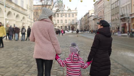 lesbian couple tourists holding hands with adoption child girl kid stay on winter city center street