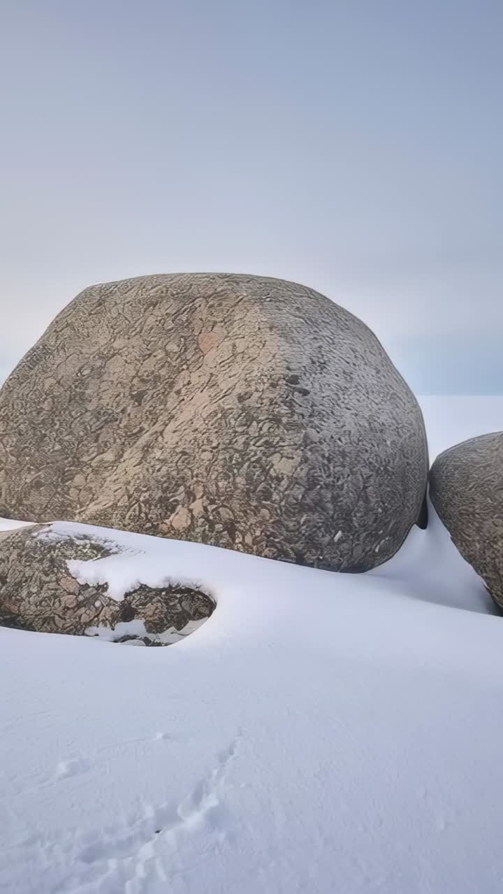 Vertikal video: Panorerende kamera, der viser samlingen mellem kampesten på en sneklædt slette for at afsløre havet, prints