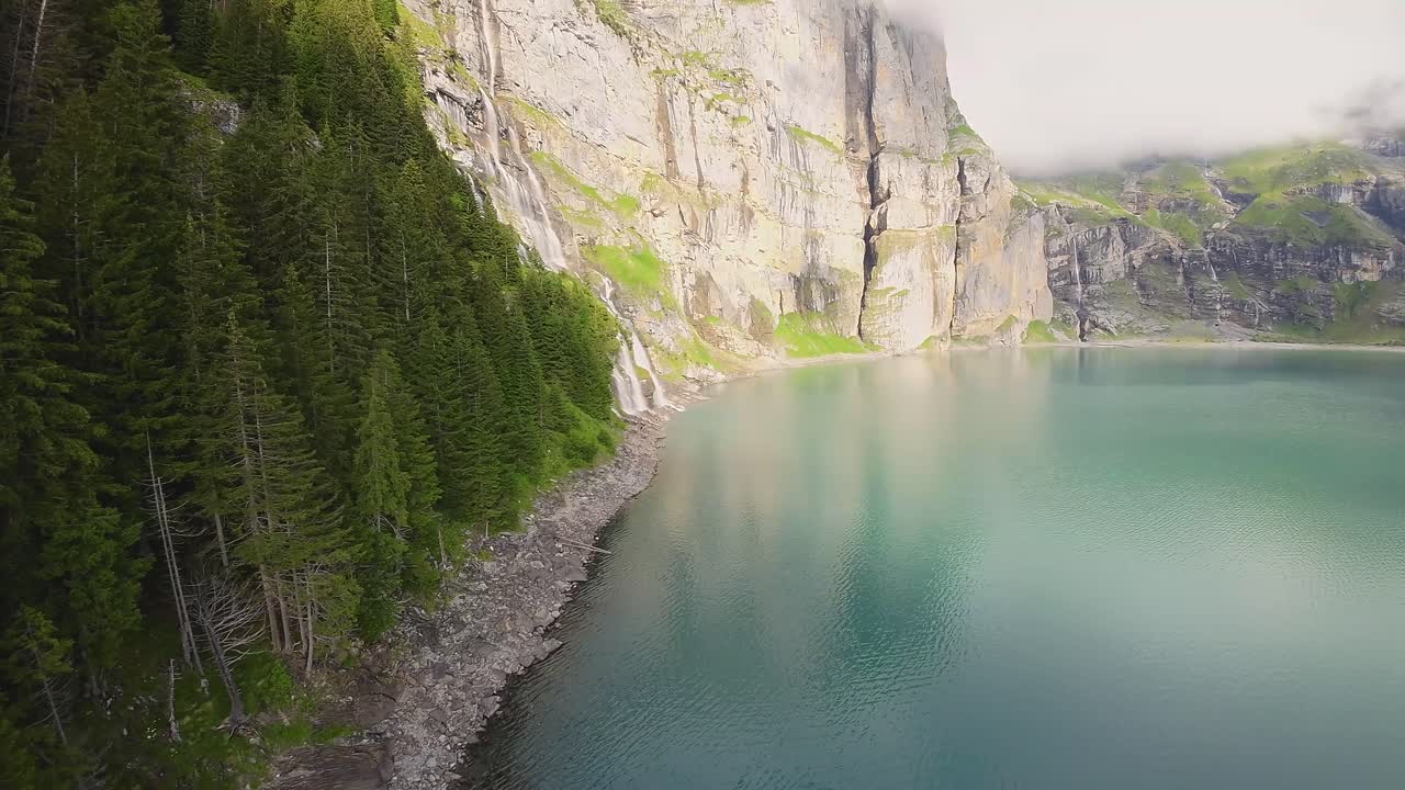 Volo aereo verso una grande e bellissima cascata in un paesaggio montano, drone che sorvola un lago blu - Lago di Oeschinen, Svizzera