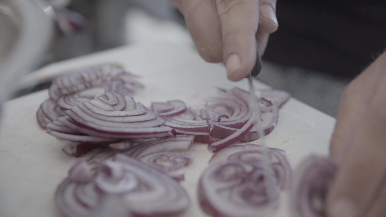 Tagliare piccoli pezzi di cipolla rossa su un tagliere da cucina bianco al rallentatore LOG.