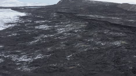 tourist sitting on snowy hill overlooking black basalt lava field at iceland volcano, aerial