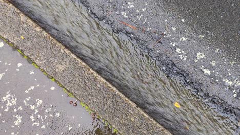 top down of fast flowing water in road side drain during heavy raining downpour on wet day