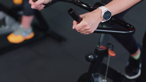 Close-up-athletic-woman-spinning-exercising-workout-on-stationary-cycling-machine-bike,-indoors