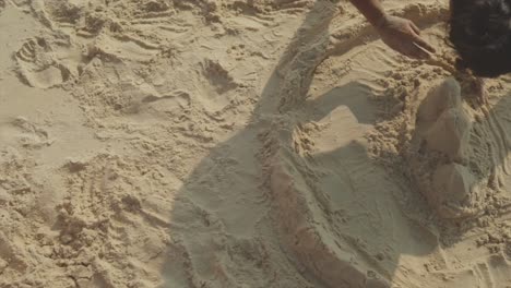 OTS-shot-of-a-girl-playing-with-the-sand-on-a-shore-and-building-a-sand-castle---A-happy-little-girl-plays-with-sand-on-the-beach