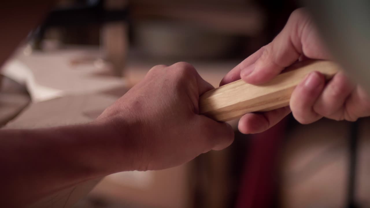Woodworker artisan carefully assembles a handcrafted wooden piece by fitting a handle into a base. Close-up shot, slow motion