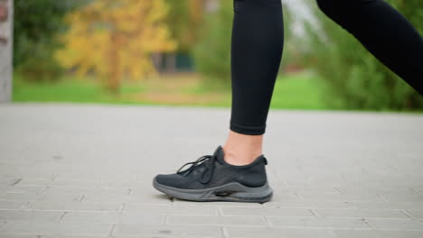 slow-motion shot of woman's leg in black sneakers walking on paved path, blurred background with flowers and bench. ideal for showcasing outdoor walking, fitness, or casual strolls in a park setting