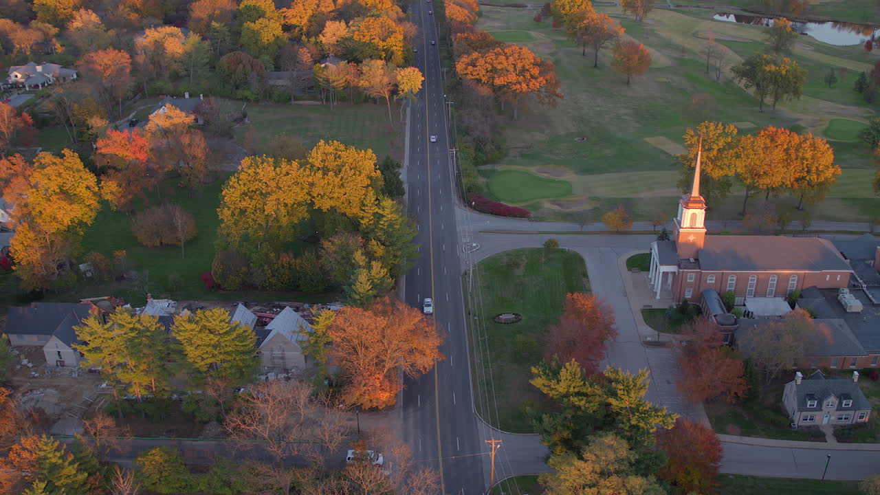 antena de un hermoso paisaje otoñal en la parte de una carretera con autos junto a árboles en el color máximo del otoño y una pequeña iglesia a la vista a la hora dorada