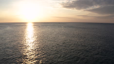 Forwarding-drone-in-middle-of-Indian-ocean-to-film-sunset-in-golden-hour-with-amazing-sunlight-reflection-with-golden-red-sun,-clouds-and-traditional-fisherman-sailing-boat-in-background-in-4k