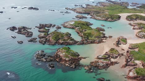 aerial orbit around cloughglass bay’s stunning grass covered rocky outcrops and a white house on the irish coastline