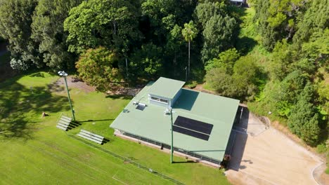 drone footage captures a lush soccer field and clubhouse surrounded by trees, under bright daylight
