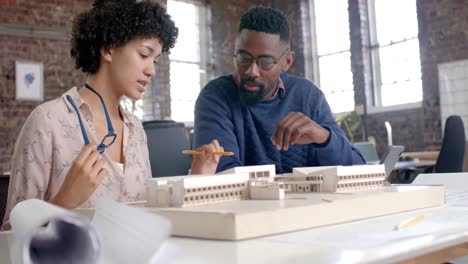 Focused-diverse-architect-colleagues-discussing-work-with-building-model-in-office-in-slow-motion