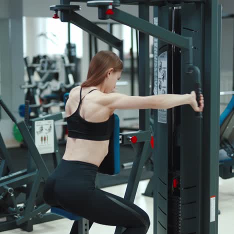 a woman with a sporty figure is sitting and doing an exercise to strengthen the back muscles in the gym. blurred background