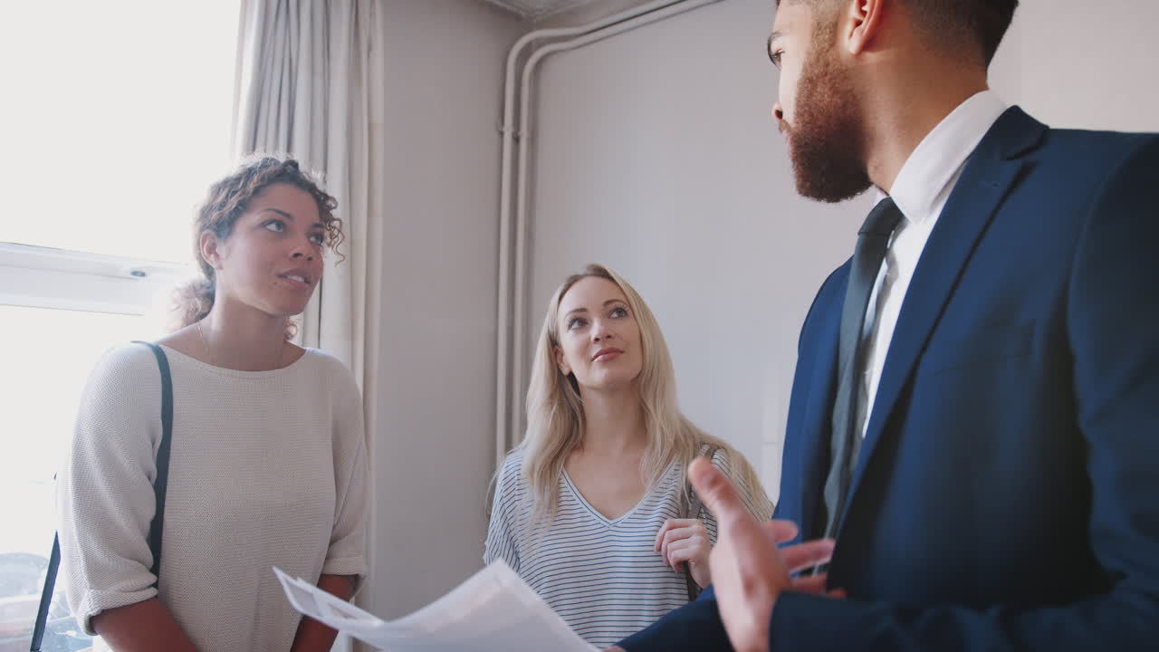 Two Female Friends Buying House For First Time Looking At House Survey With Realtor