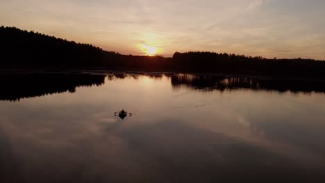 silhouette reflection with man paddling in a calm water of a lake in rogowko, poland during sunset