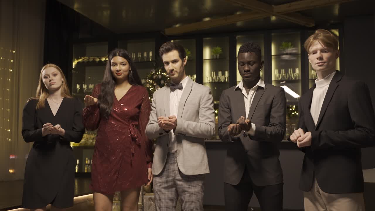 Group of friends wearing elegant clothes blow and throw conffeti while dancing in new year's party