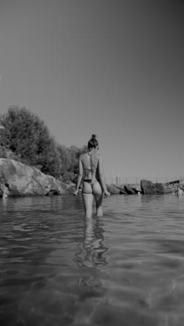 person walking into water in a bikini