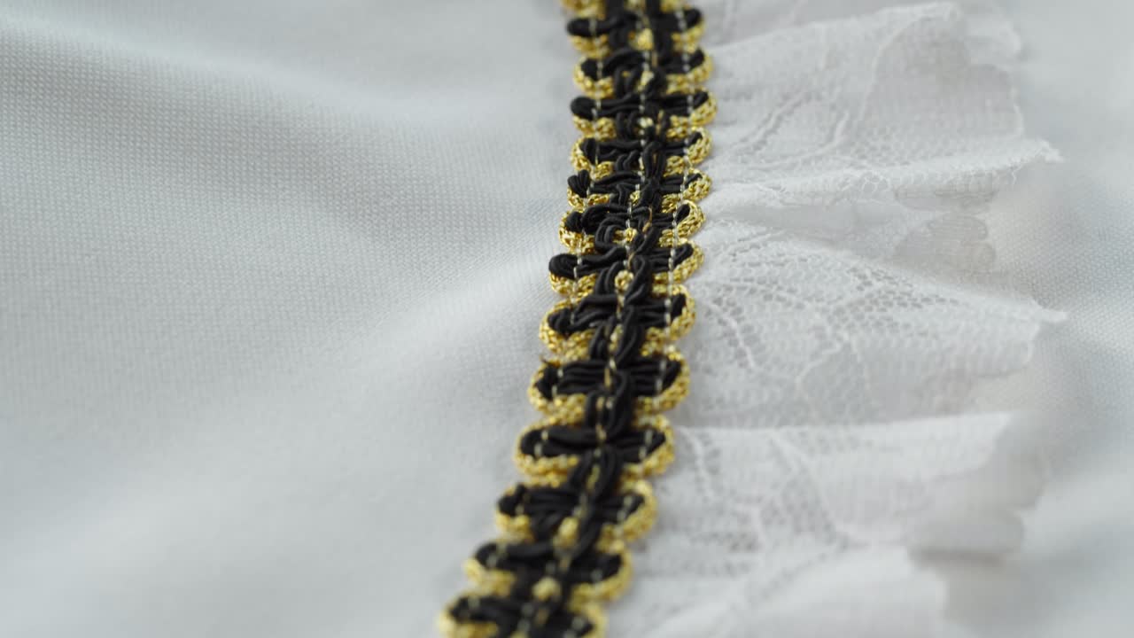 Colletto festivo. Pizzo bianco con decorazioni nere e dorate in primo piano. Cucitura di un abito da sposa. Guipure leggero. Sartoria artigianale, concetto di abbigliamento professionale. Sfondo astratto.