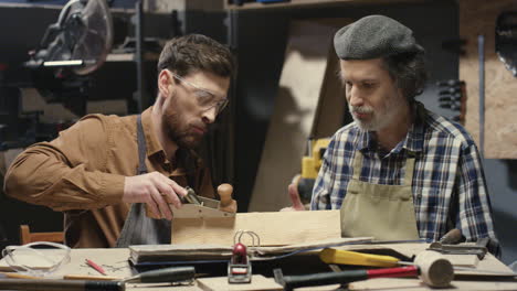 old father carpenter teaching his young son to process and work with timber in workshop