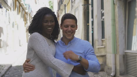 smiling multiracial couple embracing while walking on street.