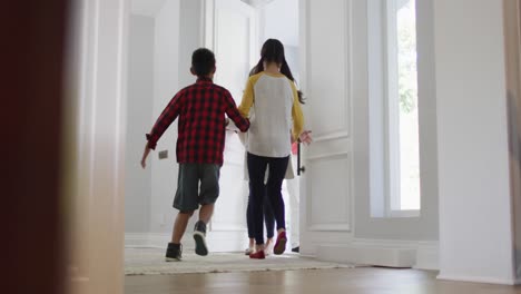 Excited-asian-son-and-daughter-at-home-running-to-greet-parents-coming-through-the-front-door