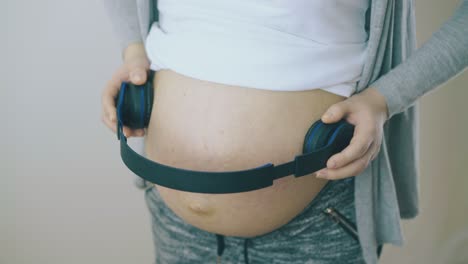 young pregnant woman with headphones on belly dances in room