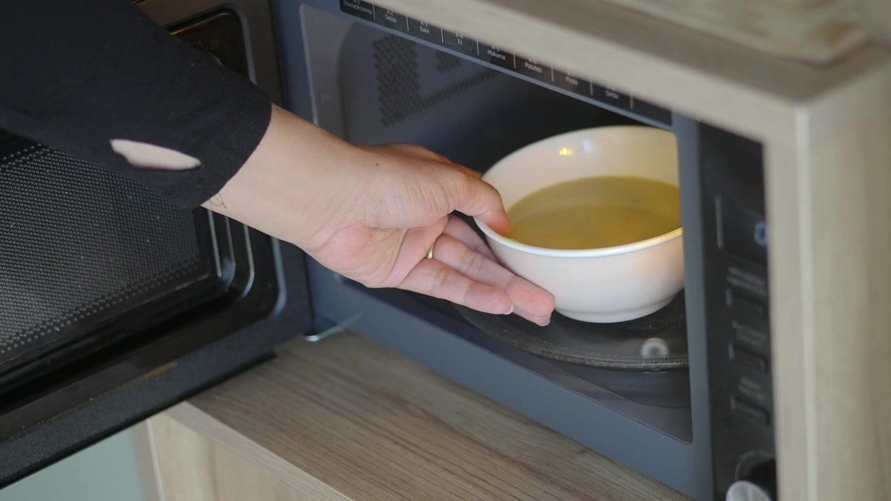 Hand Taking Bowl of Soup Out of Microwave Oven