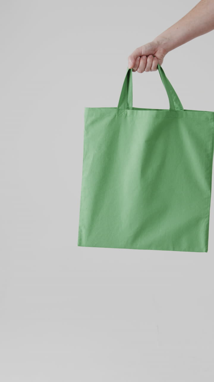 Vertical video of hand of caucasian woman with green canvas bag and copy space on white background