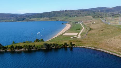 Menschen-Genießen-Den-Seestrand-Und-Seine-Gärten,-Segelboote-Segeln-An-Einem-Sonnigen-Nachmittag