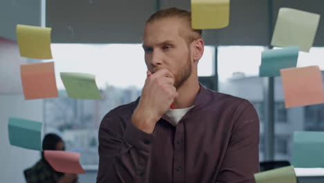 thoughtful man pondering sticker wall office closeup. startuper brainstorming