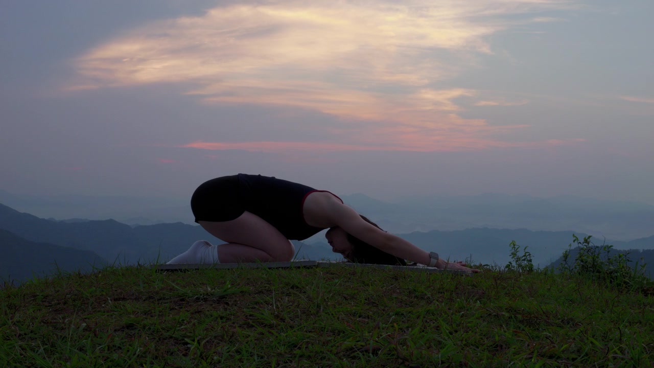 Donna che fa stretching nella posizione del bambino (asana yoga) sulla vetta di una montagna al tramonto durante una pratica di fitness all'aperto in Vietnam. Allenamento di benessere e meditazione consapevole.