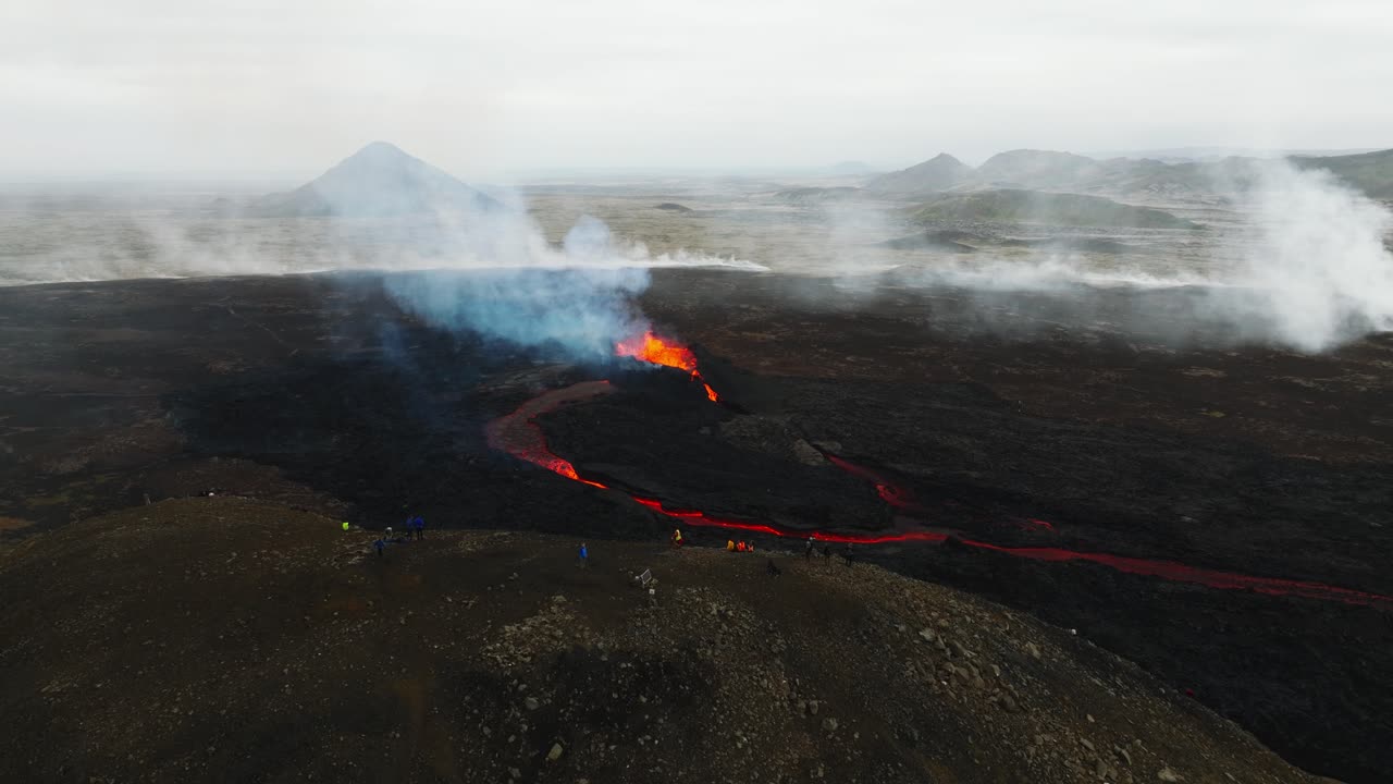 Aerial view of people looking at the volcanic eruption at Litli-Hrutur, Iceland, with lava and smoke coming out