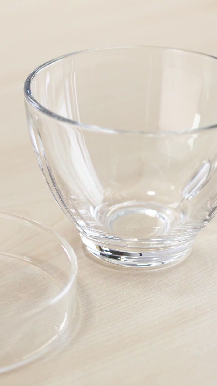 Smooth panning shot across a transparent glass teacup and saucer set on bright wood.