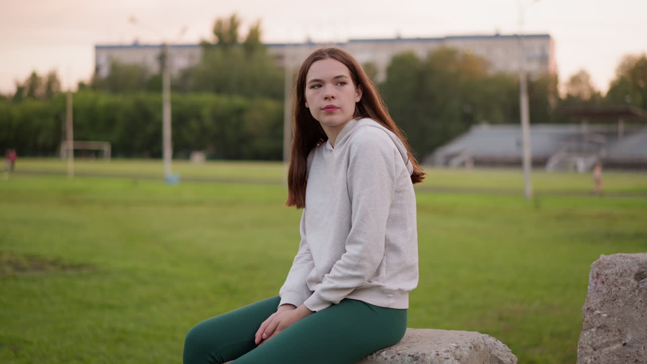 mujer descansa sentada en la piedra de hormigón del estadio. relajación en la soledad y la tristeza de la soledad por la noche. estado depresivo de la joven al atardecer