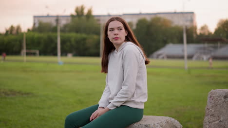 woman rests sitting on stadium concrete stone. relaxation in solitude and sadness from loneliness in evening. depressive state of young lady at sunset