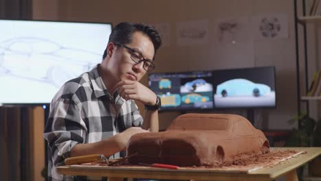 asian man automotive designer thinking about new car concept then raising his index finger while working on the sculpture of car clay in the design in the studio