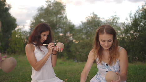 a group of young women apply patterns on clay products decorate them with tools shovels sticks in a meadow in nature in a park in an open space. camera zoom close-up.