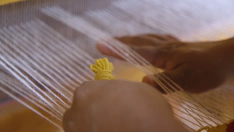 a women weaving yellow wool on a loom to create a tapestry