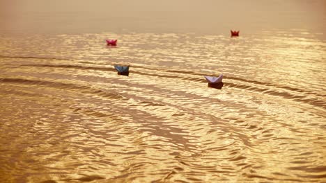 multy-colored paper boats floating on waves in a river at the evening sunset. small ships made from paper sail in water.