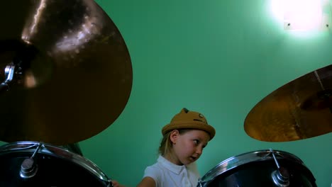 kid studying drums at music school. black drum kit. little musician drummer with drum brushes training on green wall background. blonde child girl in hat playing and smiling at lesson. 4k