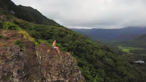 hombre solitario se sienta en un acantilado que revela el valle de kahana oahu