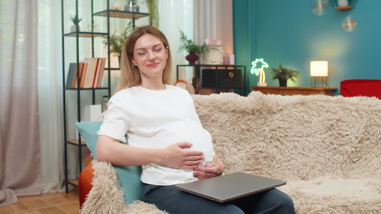 Pregnant woman closes laptop exhales relief smiles to camera rubs belly after finishing work shift