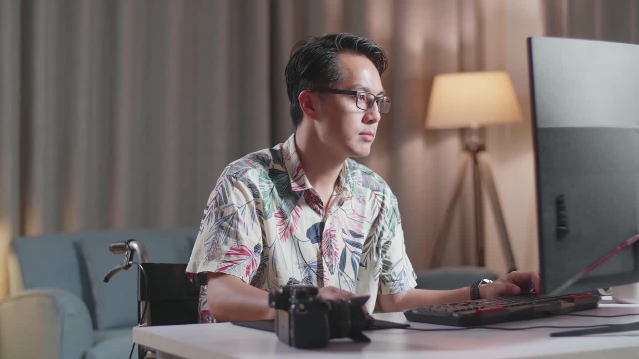 체어 에 있는 아시아인 남자 가  을 들고 집 에 있는 카메라  에 있는 데스크 으로 비디오 를 편집 하는 동안 무언가 에 대해 생각 하고 있다